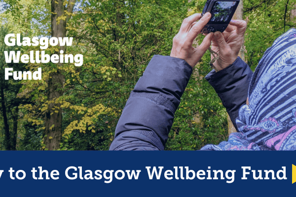 Apply to the Glasgow wellbeing fund. Photo of a women in the forest taking pictures