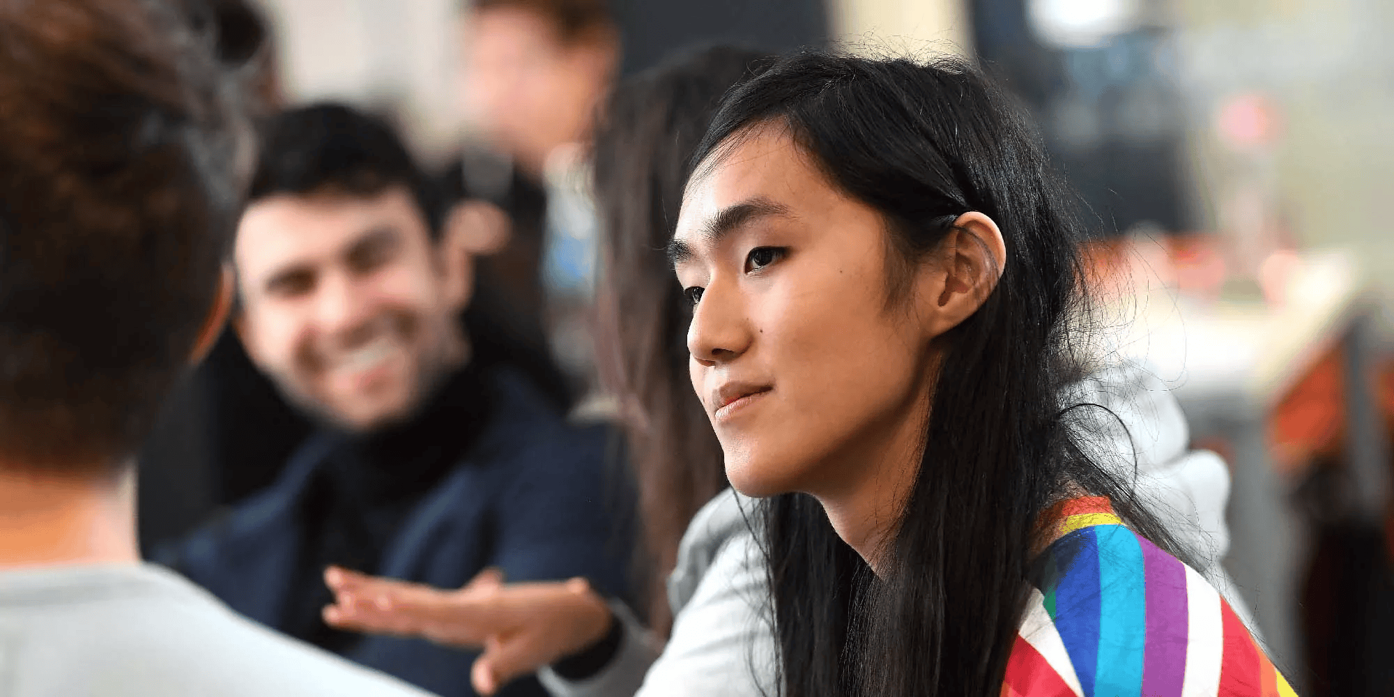 An image of a young women listening to the person next to her. A man is smiling in the background