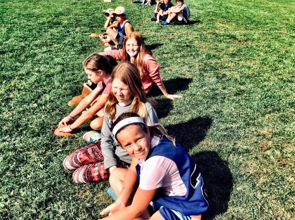 you children lined up in a row sitting on the grass in sunny weather