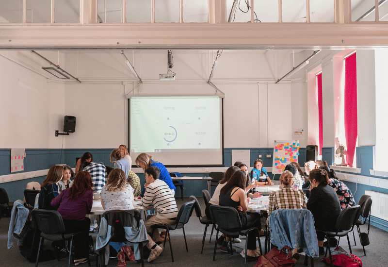 four circular tables are surrounded by people casually dressed talked to each other and making notes on the tables