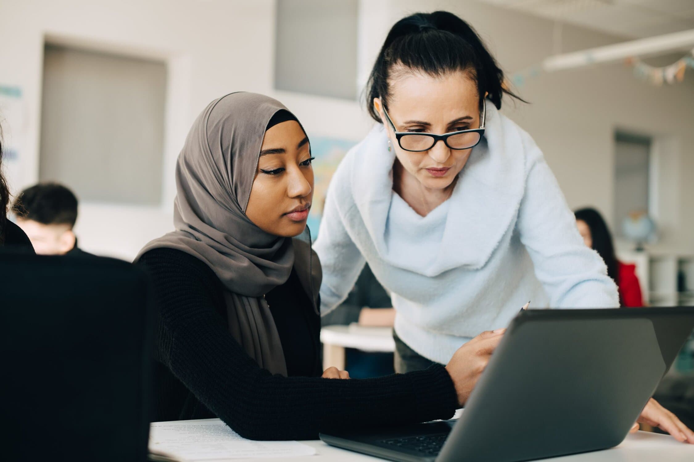 Young woman working at her computer getting help from another woman